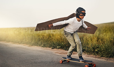 Buy stock photo Shot of a young boy pretending to fly with a pair of cardboard wings while riding a skateboard outside