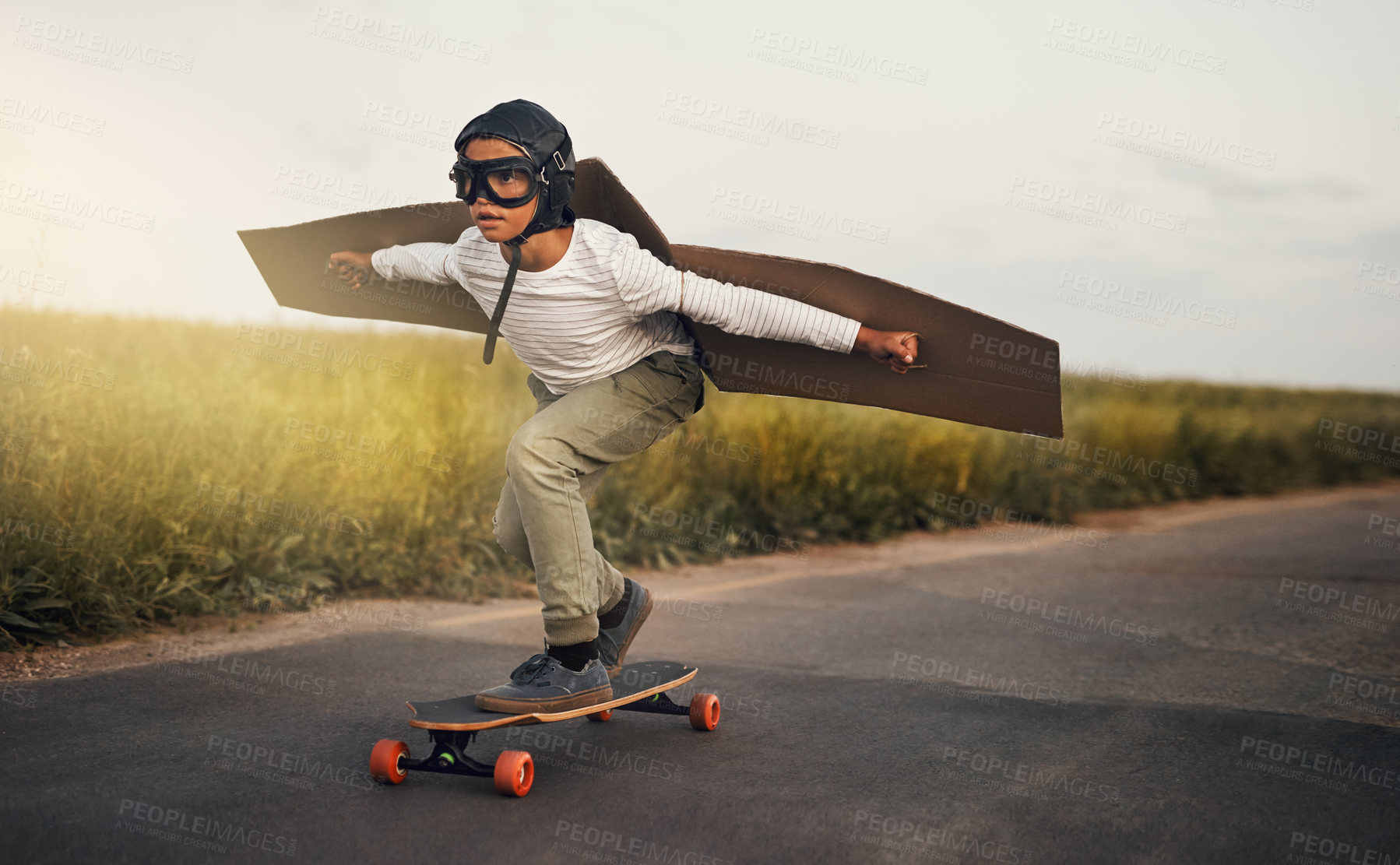 Buy stock photo Shot of a young boy pretending to fly with a pair of cardboard wings while riding a skateboard outside