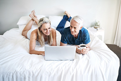 Buy stock photo Shot of a mature couple using a laptop while relaxing on their bed at home