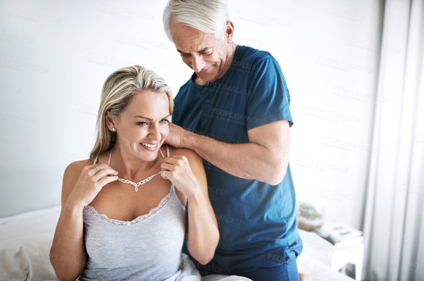 Buy stock photo Shot of a mature man putting a necklace around his wife's neck at home