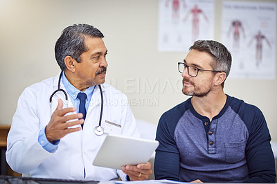Buy stock photo Shot of a confident mature male doctor seated at his desk while consulting a patient inside a hospital during the day