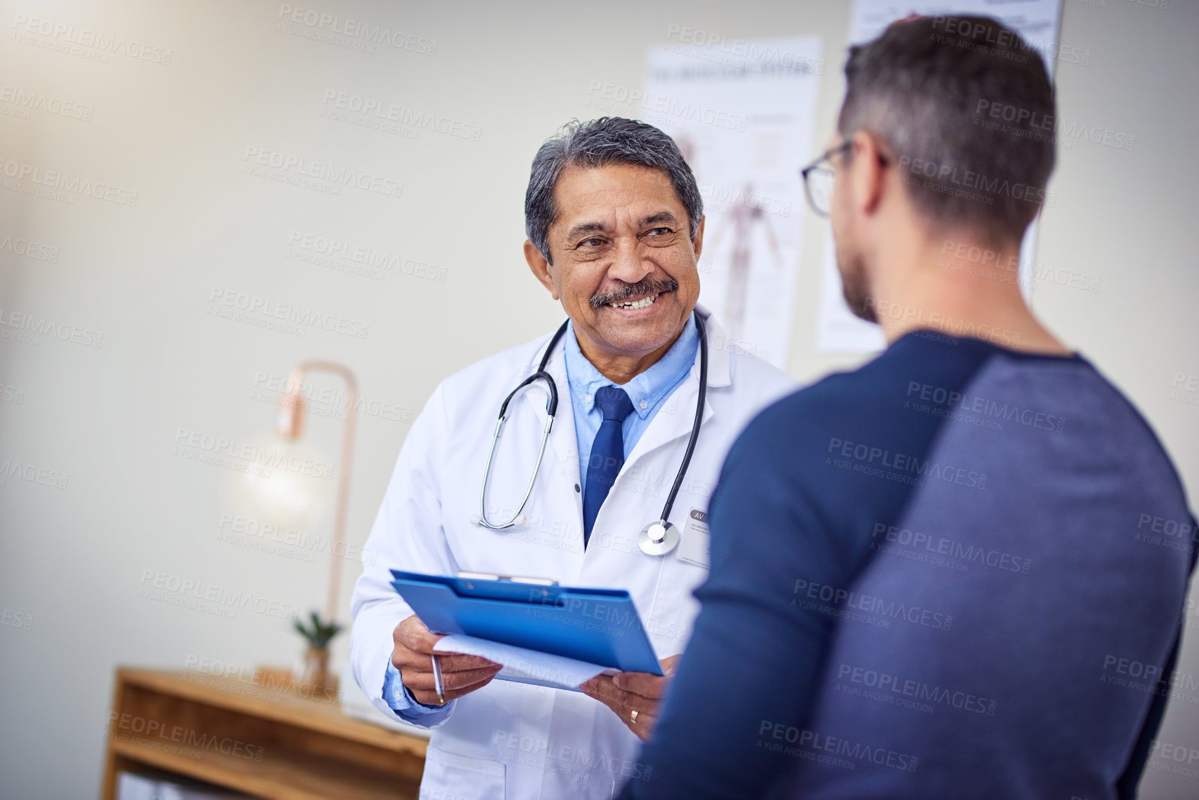 Buy stock photo Shot of a cheerful mature male doctor consulting a patient while standing inside a hospital during the day