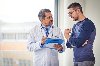 Buy stock photo Shot of a confident mature male doctor consulting a patient while standing inside a hospital during the day