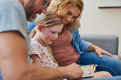 Buy stock photo Cropped shot of a mother and father reading a book with their daughter on the sofa at home
