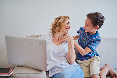 Buy stock photo Cropped shot of a mother using a laptop while her son surprises her on the sofa at home
