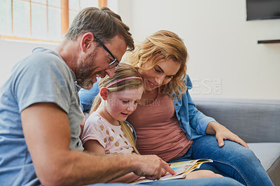 Buy stock photo Cropped shot of a mother and father reading a book with their daughter on the sofa at home