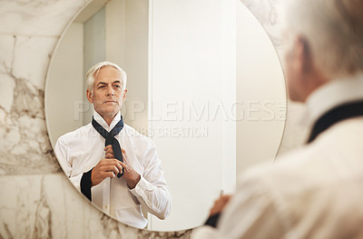 Buy stock photo Shot of an confident mature businessman looking at his reflection in a mirror while getting dressed at home during the day
