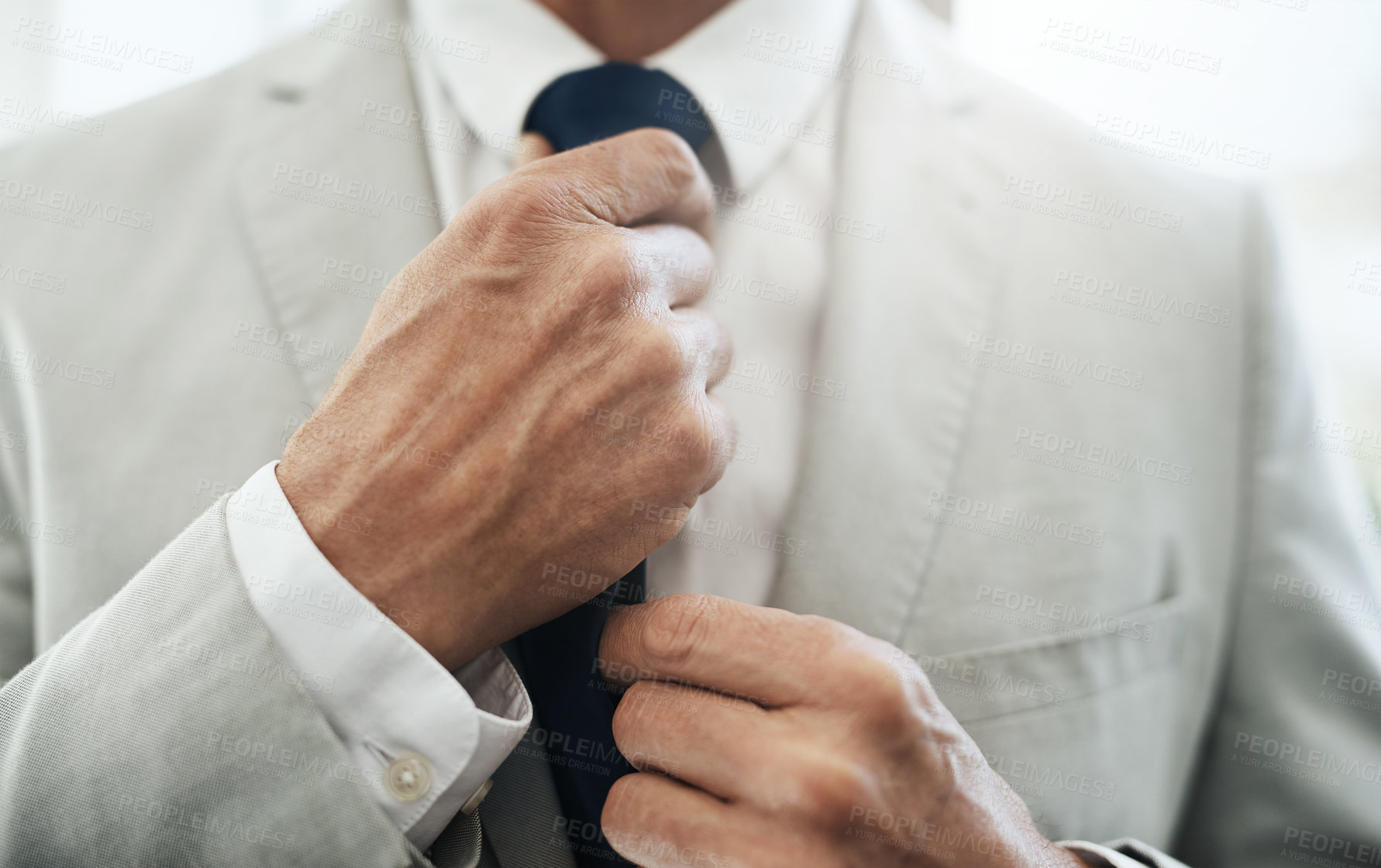 Buy stock photo Shot of an unrecognizable businessman wearing a business suit while adjusting his tie before going out to work at home during the day