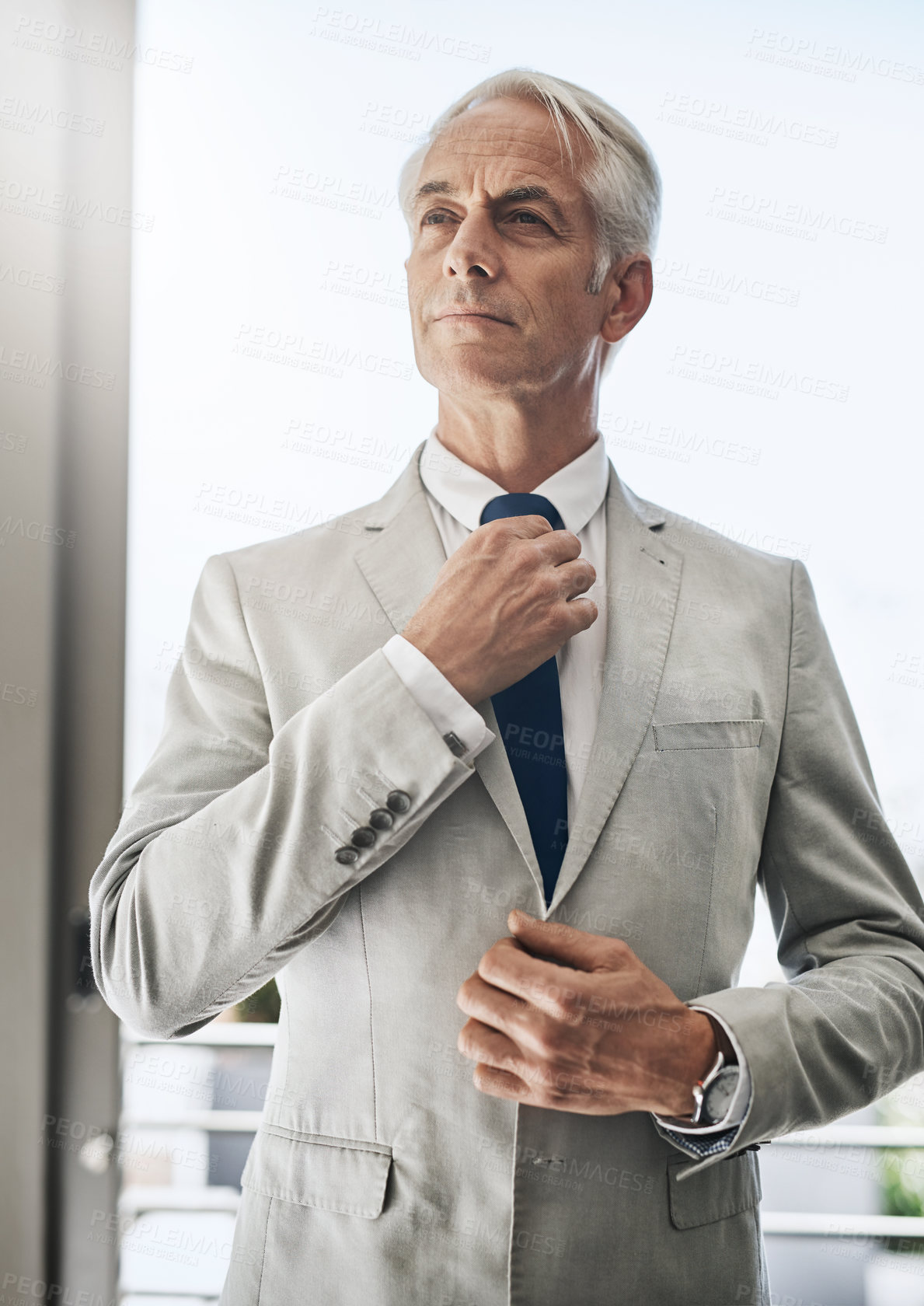 Buy stock photo Shot of a confident mature businessman wearing a business suit while adjusting his tie before going out to work at home during the day