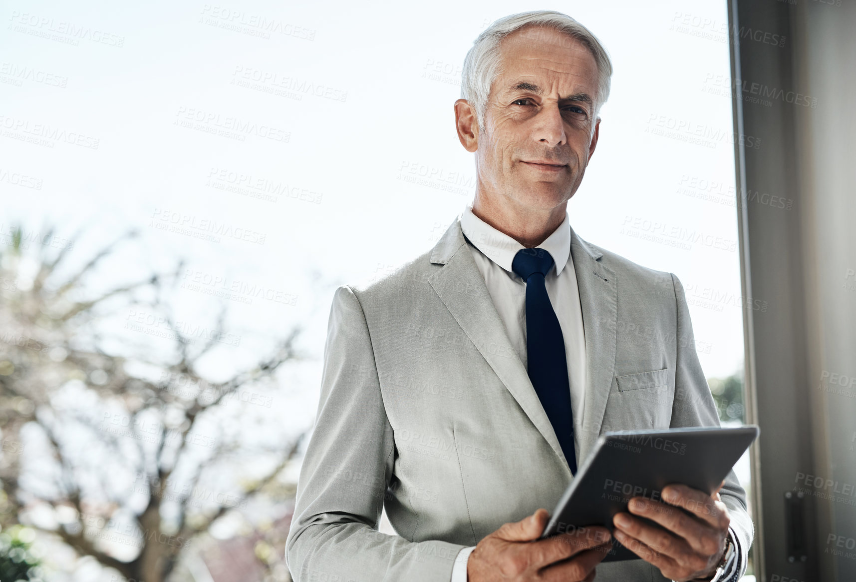 Buy stock photo Portrait of a confident mature businessman wearing a business suit while browsing on a digital tablet at home during the day
