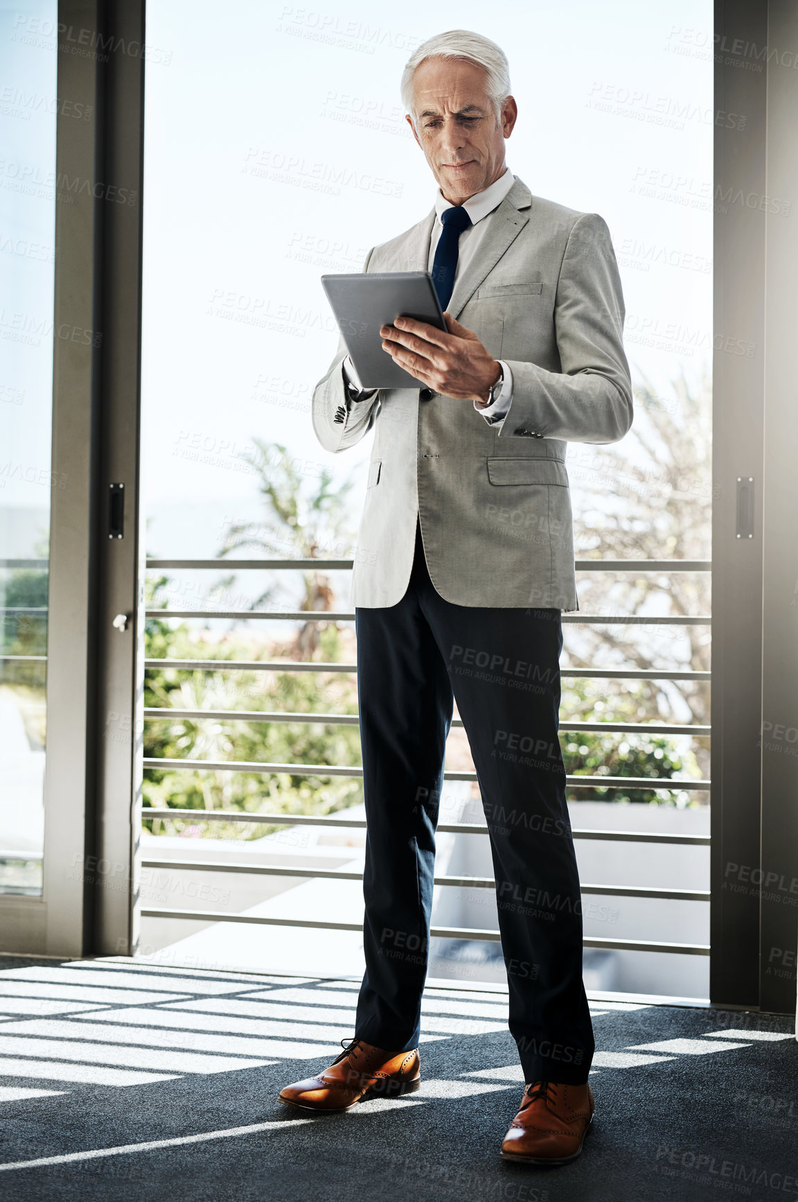 Buy stock photo Shot of a confident mature man wearing a business suit while browsing on a digital tablet at home during the day