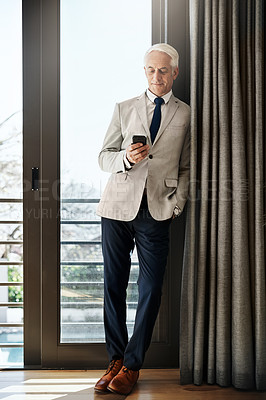 Buy stock photo Shot of a cheerful mature businessman standing with his one hand in his pocket while texting on his phone inside of a house during the day