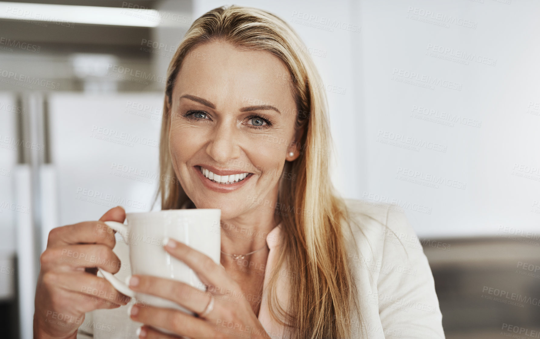 Buy stock photo Portrait of a cheerful middle aged businesswoman seated behind a counter while drinking a cup of coffee inside of a kitchen during the day