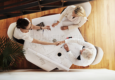 Buy stock photo High angle shot of a group of architects working together on blueprints of a house around a table while shaking hands in agreement inside of a building