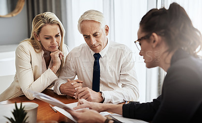 Buy stock photo Shot of a focused mature couple negotiating with a architect over house plans around a table inside of a building during the day