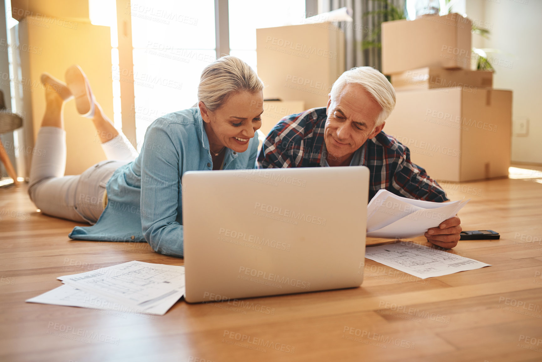 Buy stock photo Shot of a mature couple using a laptop and going through paperwork together on moving day