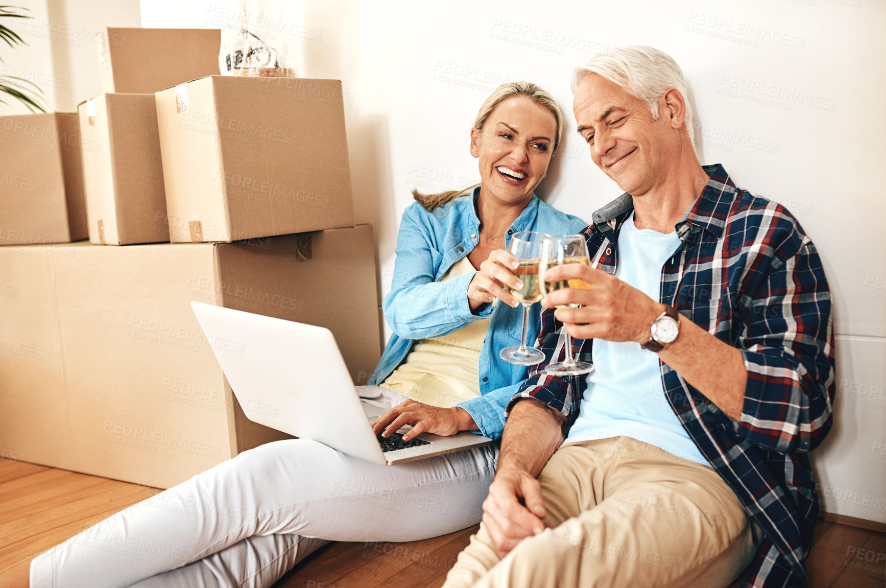 Buy stock photo Shot of a happy mature couple using a laptop and drinking wine together on moving day