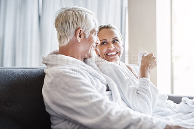 Buy stock photo Shot of a cheerful middle aged couple relaxing together while wearing bathrobes and sitting on a couch inside of a spa during the day