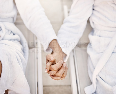 Buy stock photo Shot of two unrecognizable people holding hands while relaxing in bathrobes outside at a spa during the day
