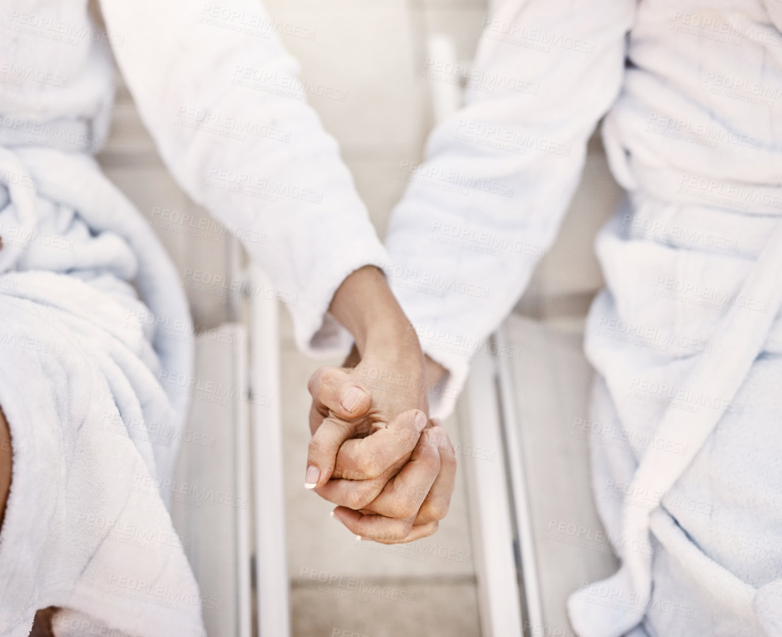 Buy stock photo Shot of two unrecognizable people holding hands while relaxing in bathrobes outside at a spa during the day