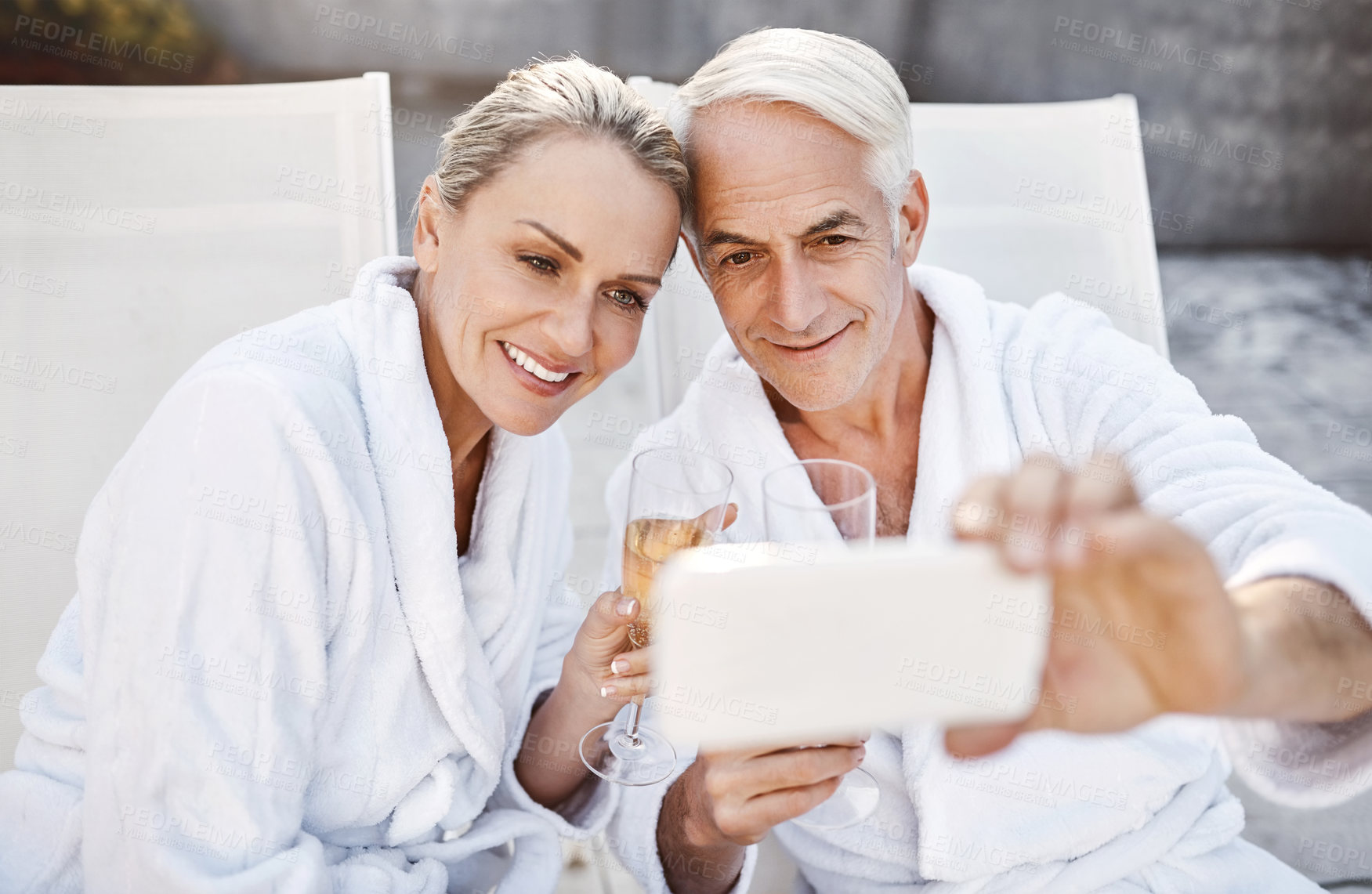 Buy stock photo Shot of a cheerful middle aged couple taking a self portrait together while enjoying a glass of champagne outside at a spa during the day
