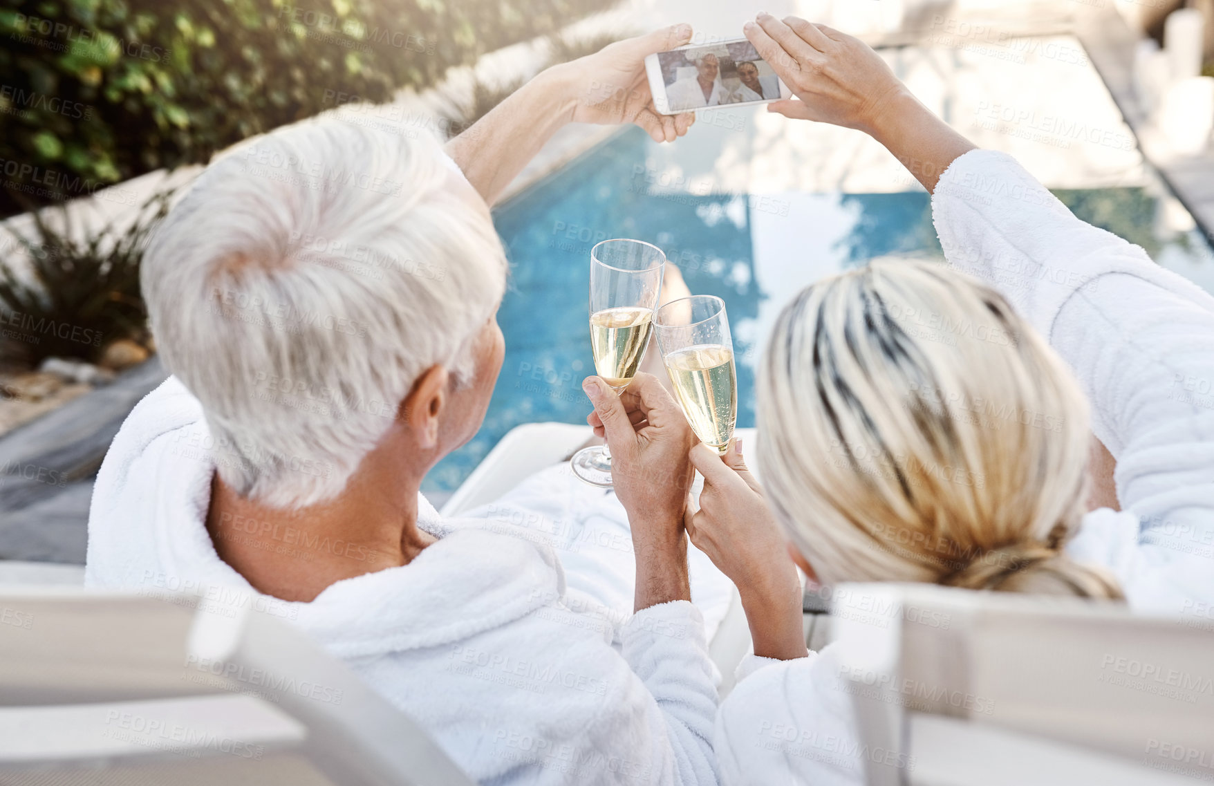 Buy stock photo Rearview shot of a cheerful middle aged couple having a celebratory toast with champagne outside during the day