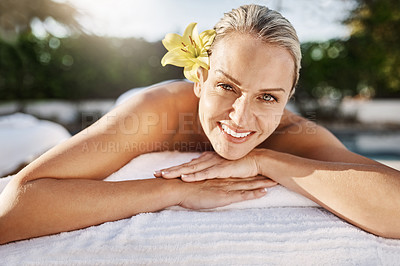 Buy stock photo Portrait of a cheerful middle aged woman lying on her stomach waiting to get a massage at a spa outside during the day