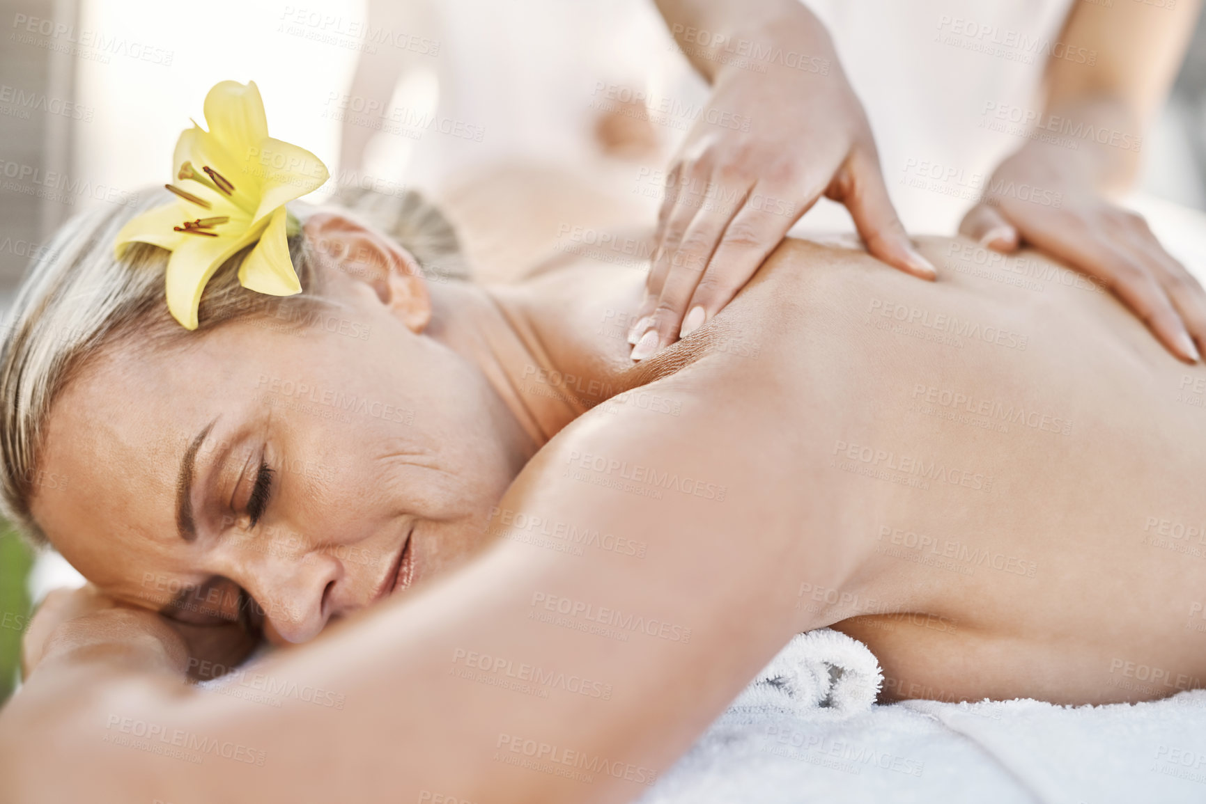 Buy stock photo Shot of a relaxed middle aged woman lying on her stomach while receiving a massage at a spa outside during the day