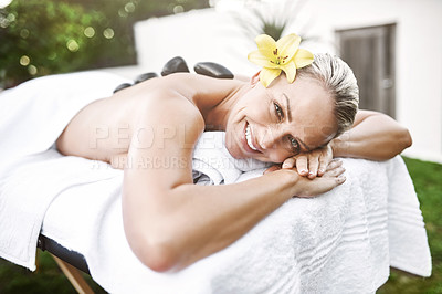 Buy stock photo Portrait of a relaxed middle aged woman lying on a massage bed with warm stones on her back at a spa during the day