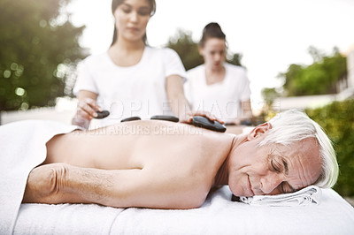 Buy stock photo Shot of a relaxed middle aged man lying on his stomach while receiving a massage at a spa outside during the day