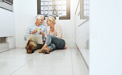Buy stock photo Full length shot of an affectionate mature couple drinking wine while browsing the web on their kitchen floor