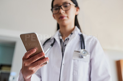 Buy stock photo Low angle shot of a young female doctor sending a text while working in the hospital