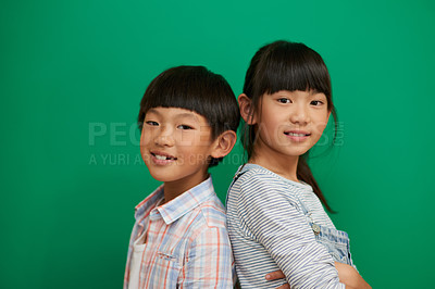 Buy stock photo Studio portrait of two cheerful children standing with their backs against each other next to a green background