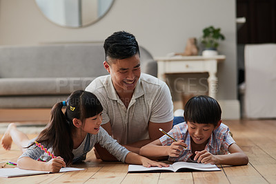 Buy stock photo Shot of a cheerful father and his two children doing homework together while lying on the floor at home during the day