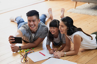 Buy stock photo Shot of a cheerful mother and father doing homework with their little girl while taking a self portrait at home during the day