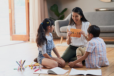 Buy stock photo Shot of a cheerful mother and her two children doing homework together while seated on the floor at home during the day
