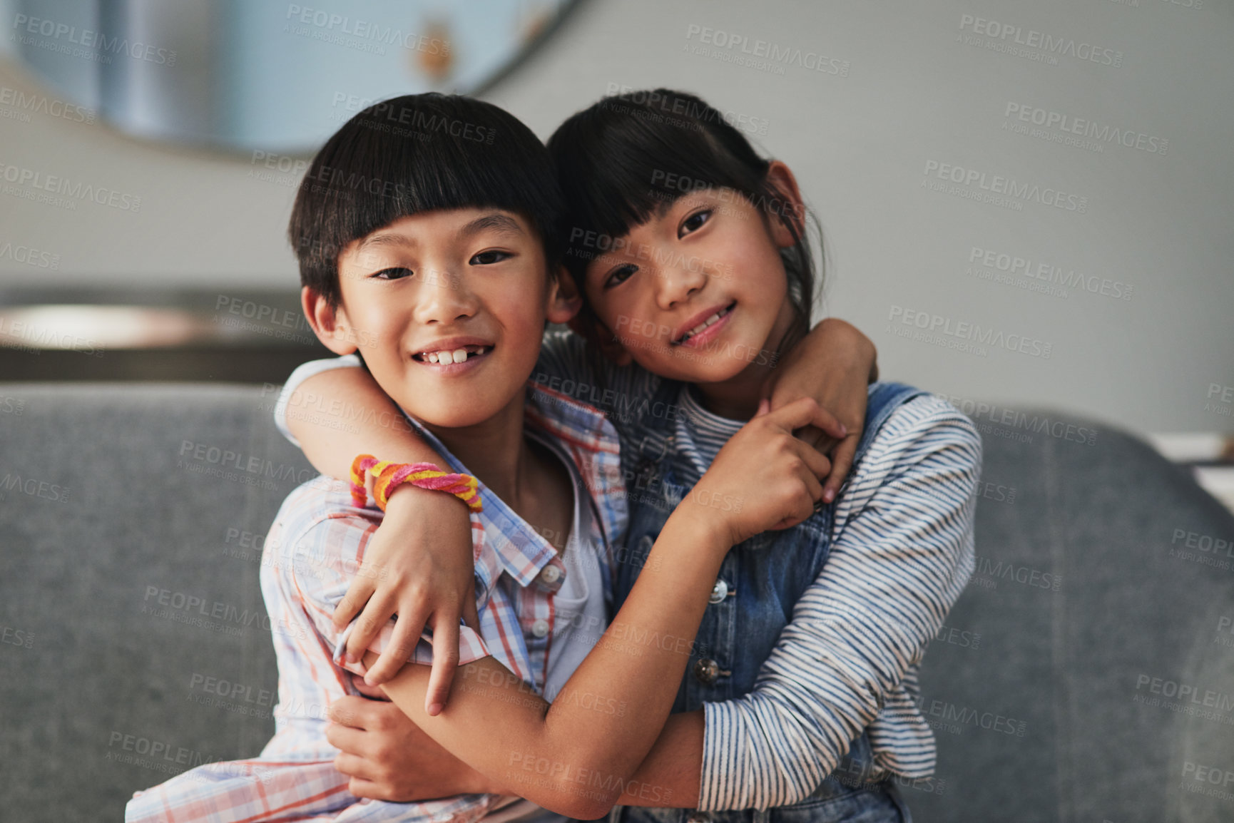 Buy stock photo Portrait of a cheerful brother and sister holding each other while being seated on a couch at home during the day