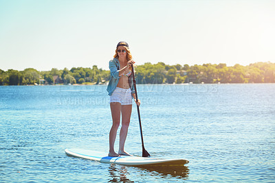 Buy stock photo Shot of an attractive young woman paddle boarding on a lake