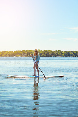 Buy stock photo Shot of an attractive young woman paddle boarding on a lake