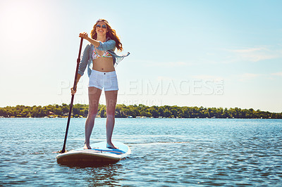 Buy stock photo Shot of an attractive young woman paddle boarding on a lake