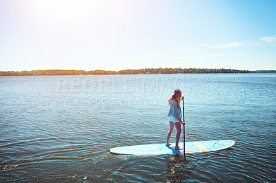 Buy stock photo Shot of an attractive young woman paddle boarding on a lake