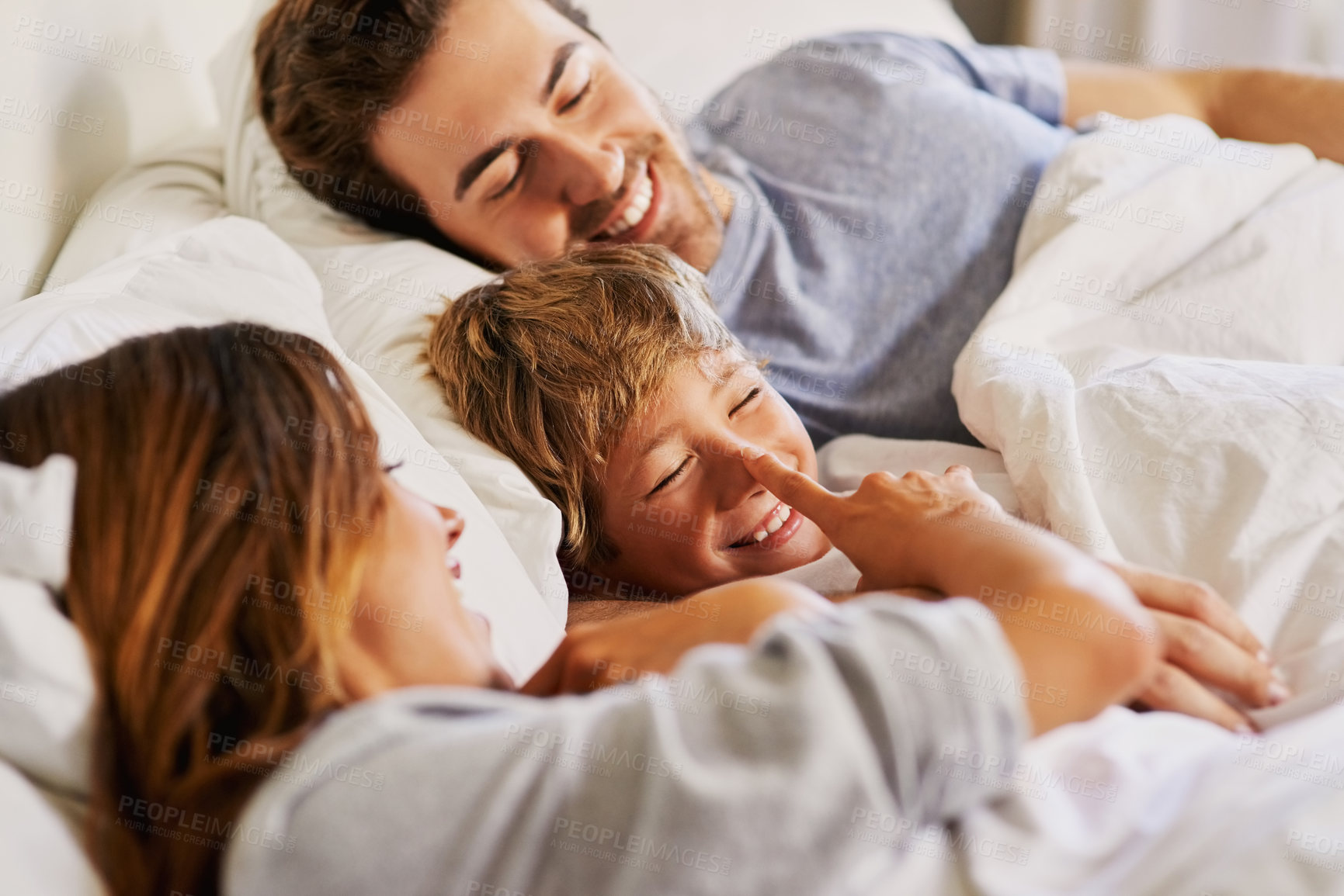 Buy stock photo Shot of a cheerful young family relaxing in bed at home during the day