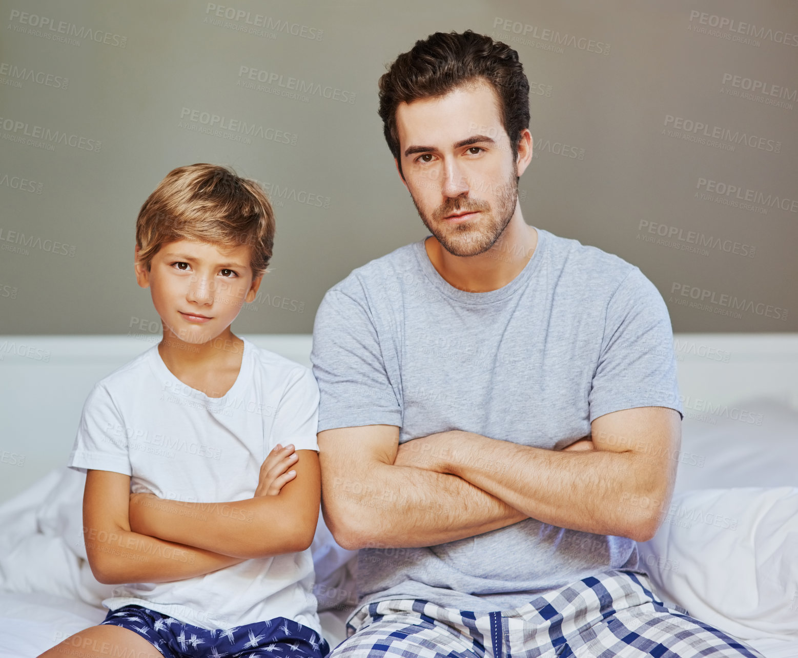 Buy stock photo Portrait of a confident father and son seated on a bed with arms folded while looking at the camera at home in the morning