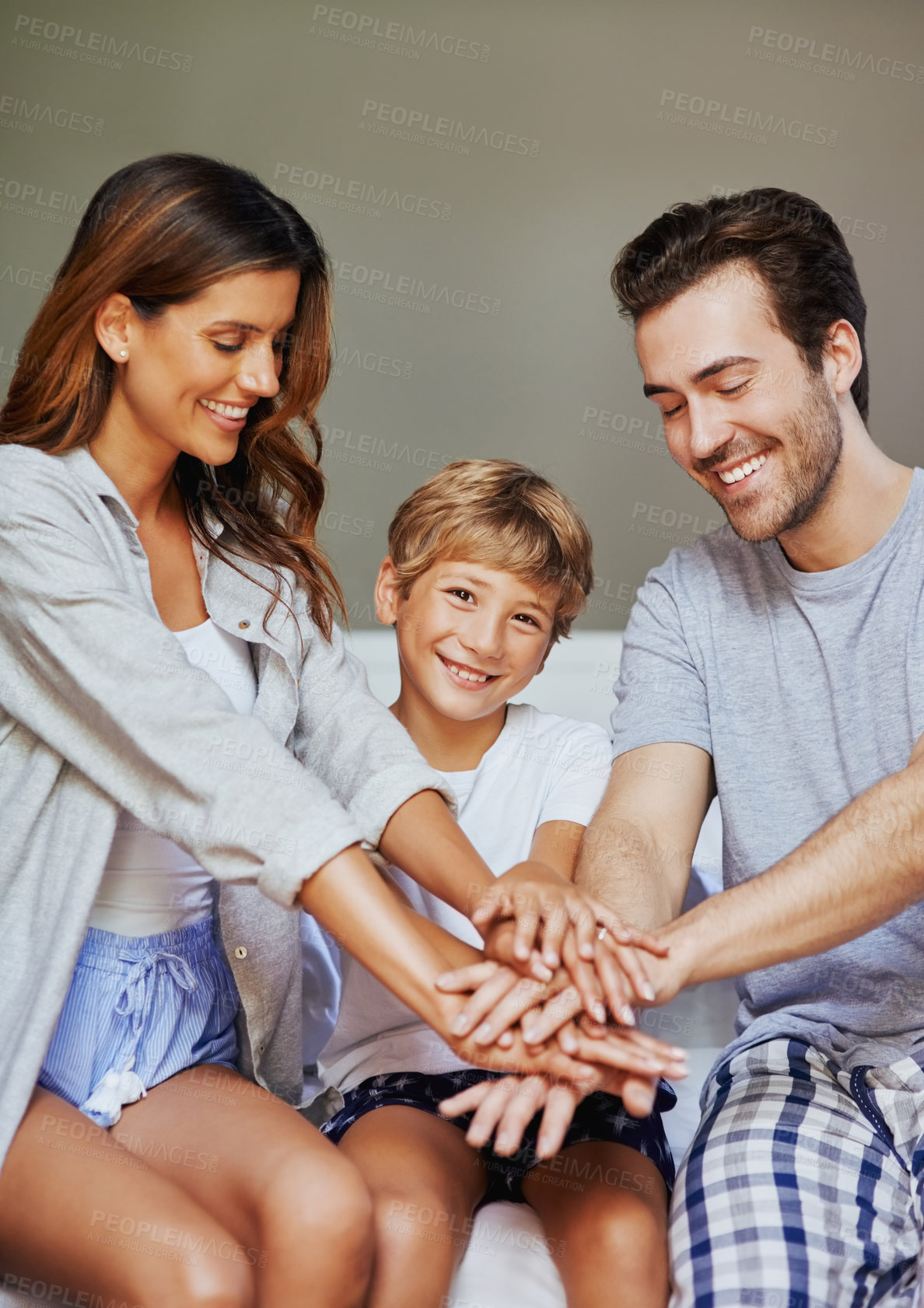 Buy stock photo Shot of a cheerful young family forming a huddle with their hands while being seated in the bedroom at home in the morning