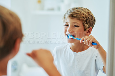 Buy stock photo Shot of a cheerful young boy looking at his reflection in a mirror while brushing his teeth in the bathroom at home during the day
