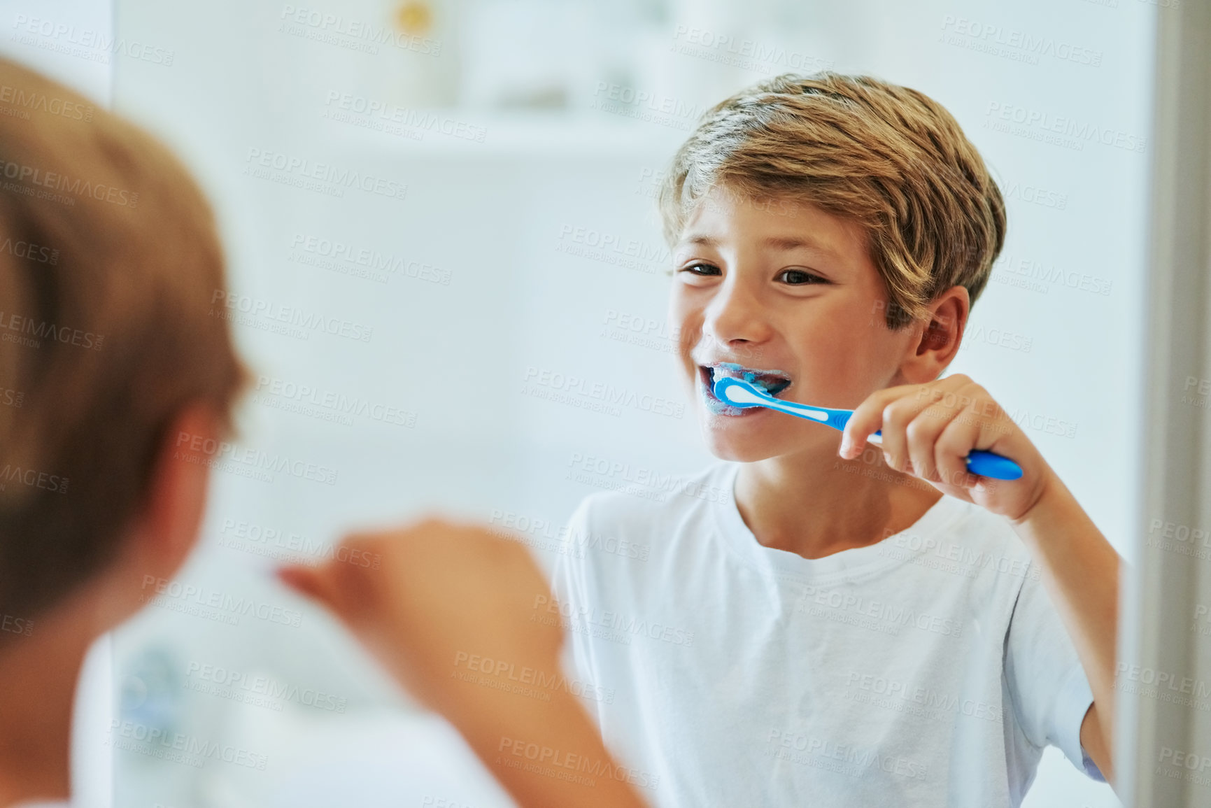 Buy stock photo Shot of a cheerful young boy looking at his reflection in a mirror while brushing his teeth in the bathroom at home during the day