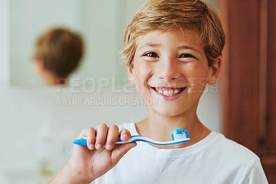Buy stock photo Portrait of a cheerful young boy looking at his reflection in a mirror while brushing his teeth in the bathroom at home during the day