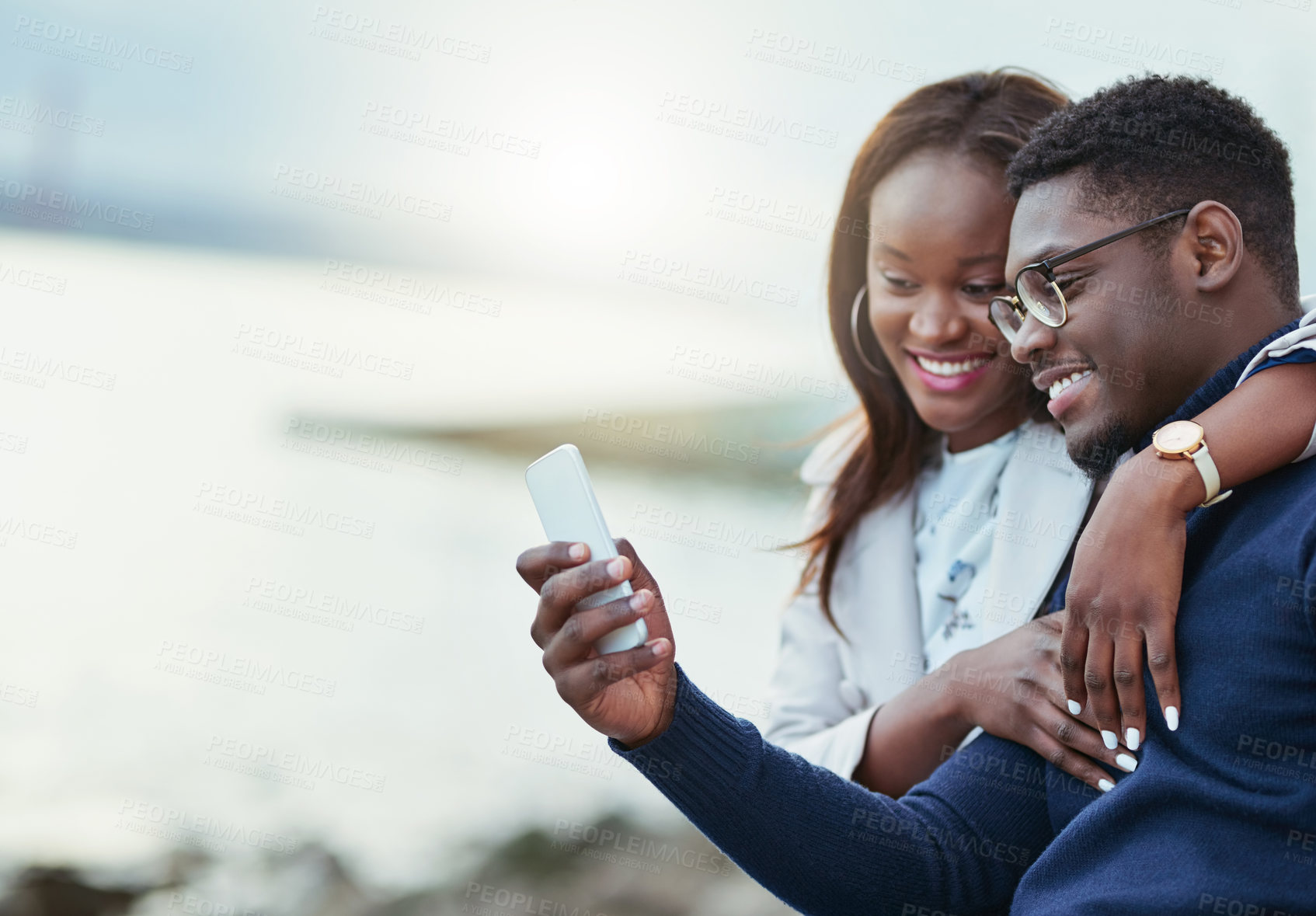Buy stock photo Shot of an affectionate young couple using a cellphone together outdoors