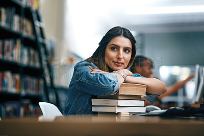 Buy stock photo Shot of a young woman resting on a pile of books in a college library and looking thoughtful