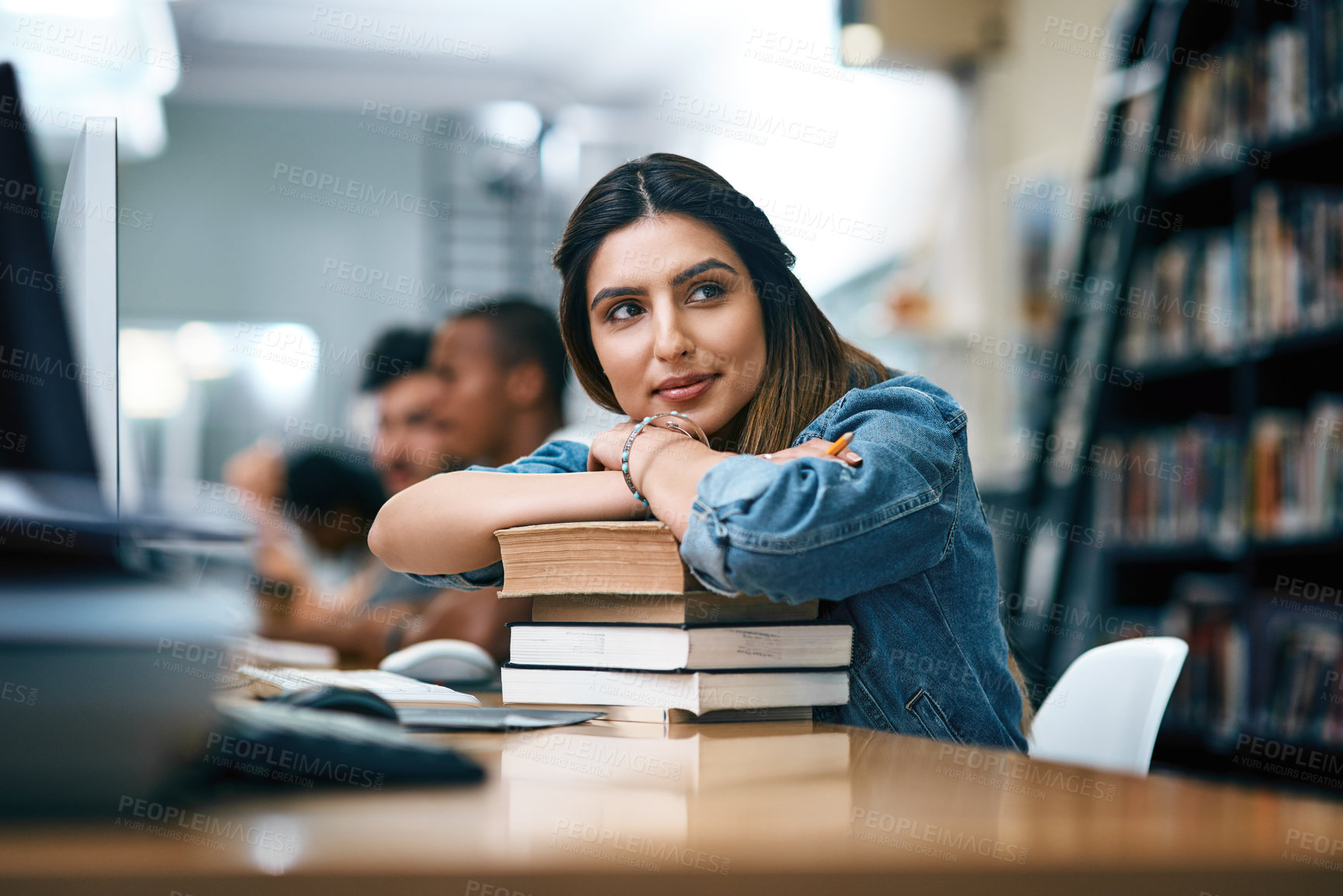 Buy stock photo Shot of a young woman resting on a pile of books in a college library and looking thoughtful